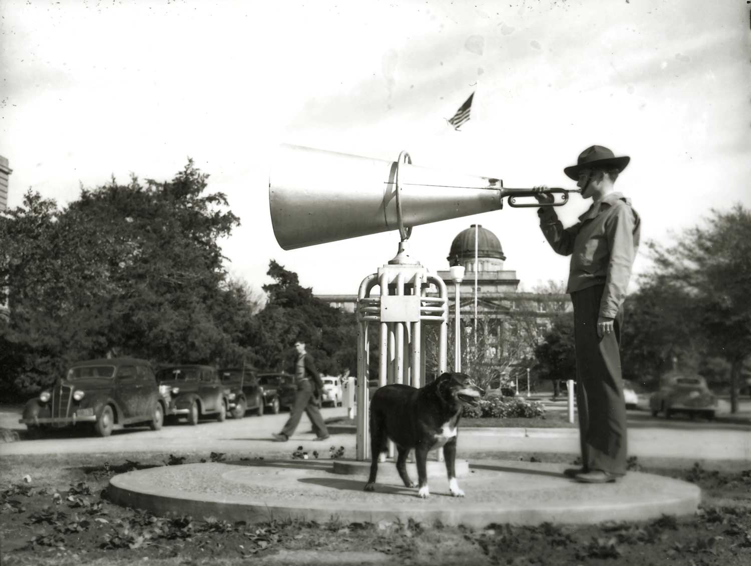 Cadet blowing a bugle while an early reveille stands in front of him