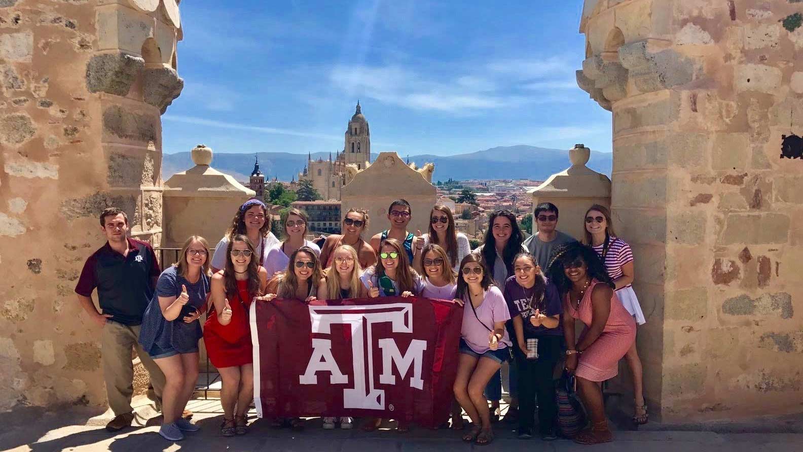 Study abroad students hold up a Texas A&M flag while taking a picture in their host country