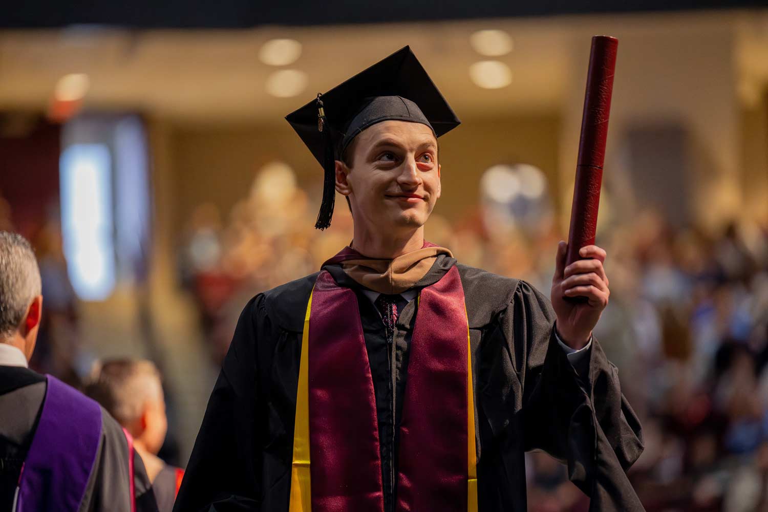 Student holds up his diploma tube at graduation