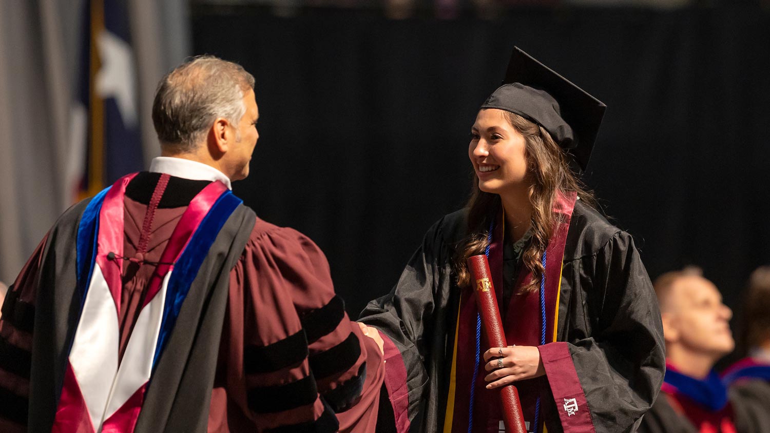 Student shakes a professors hand as she receives her diploma at graduation
