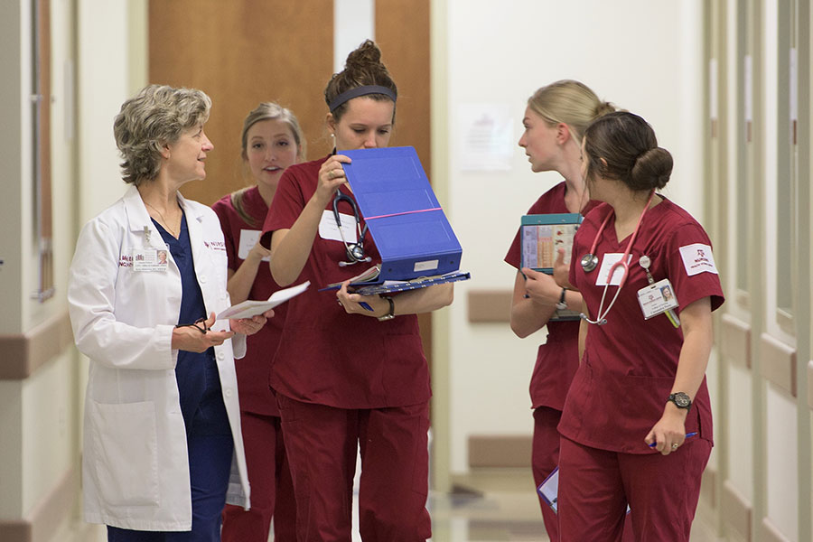 School of Nursing students walk with their professor and look over clinical notes after class