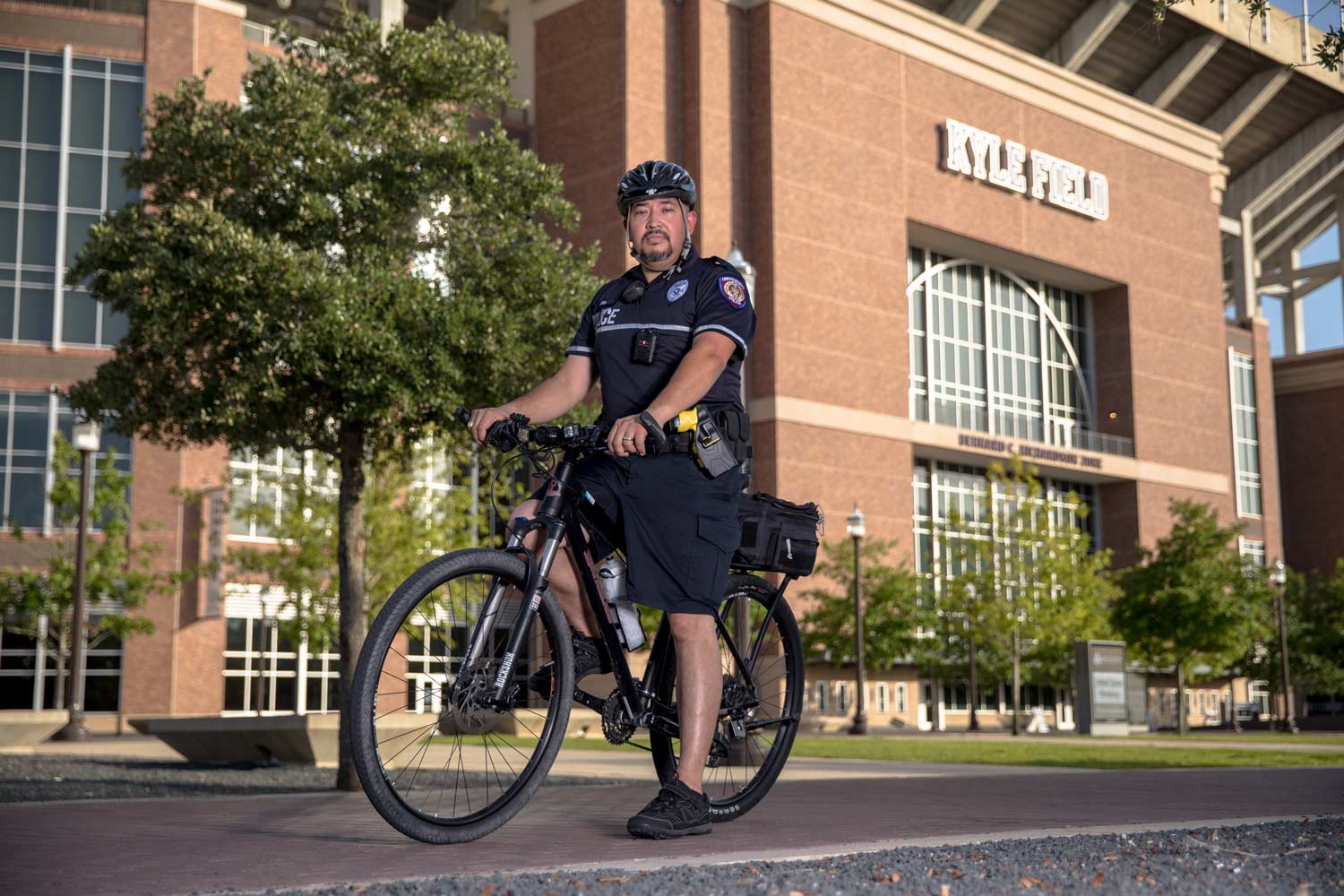 University police officer posing on a bicycle in front of Kyle Field on campus.