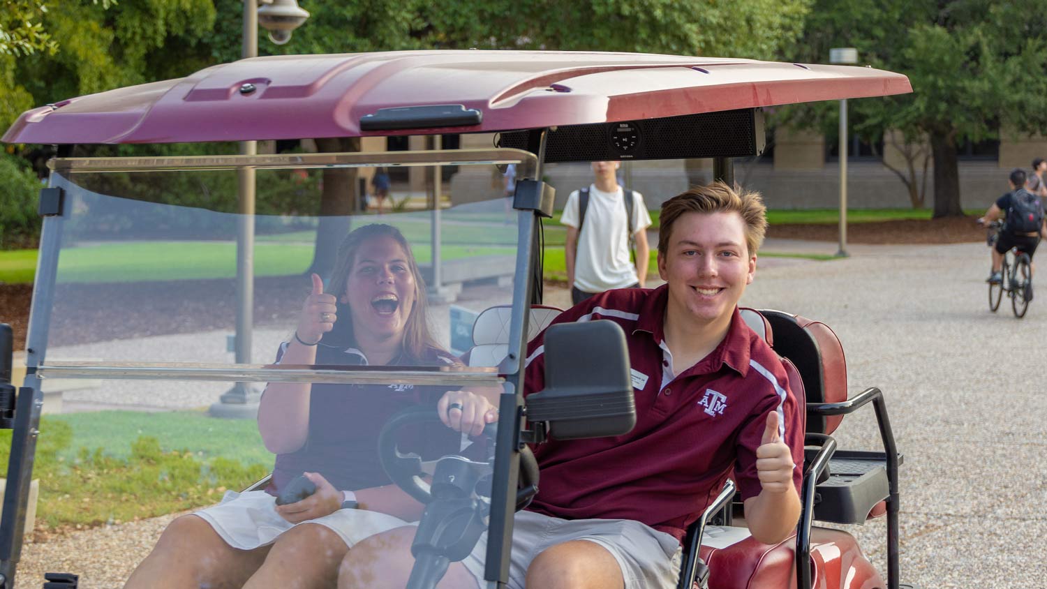 Two Howdy Crew tour guides from the Visitor Center smile from a golf cart as the drive across campus
