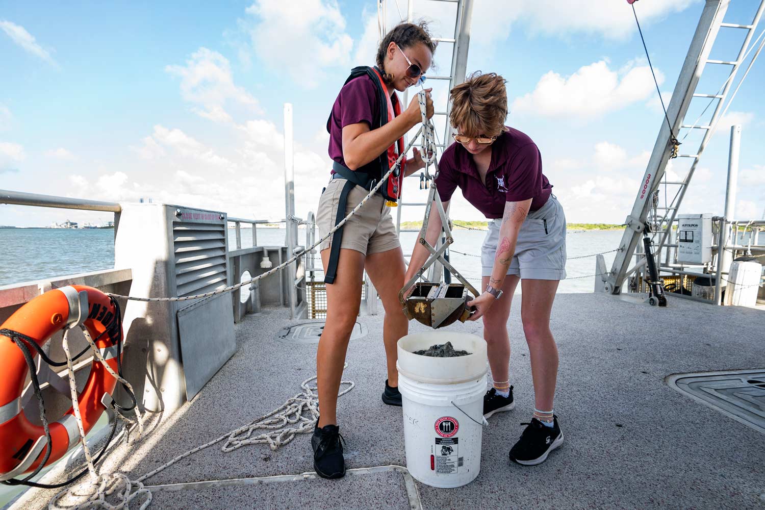 Two students sifting material into a bucket on a boat.