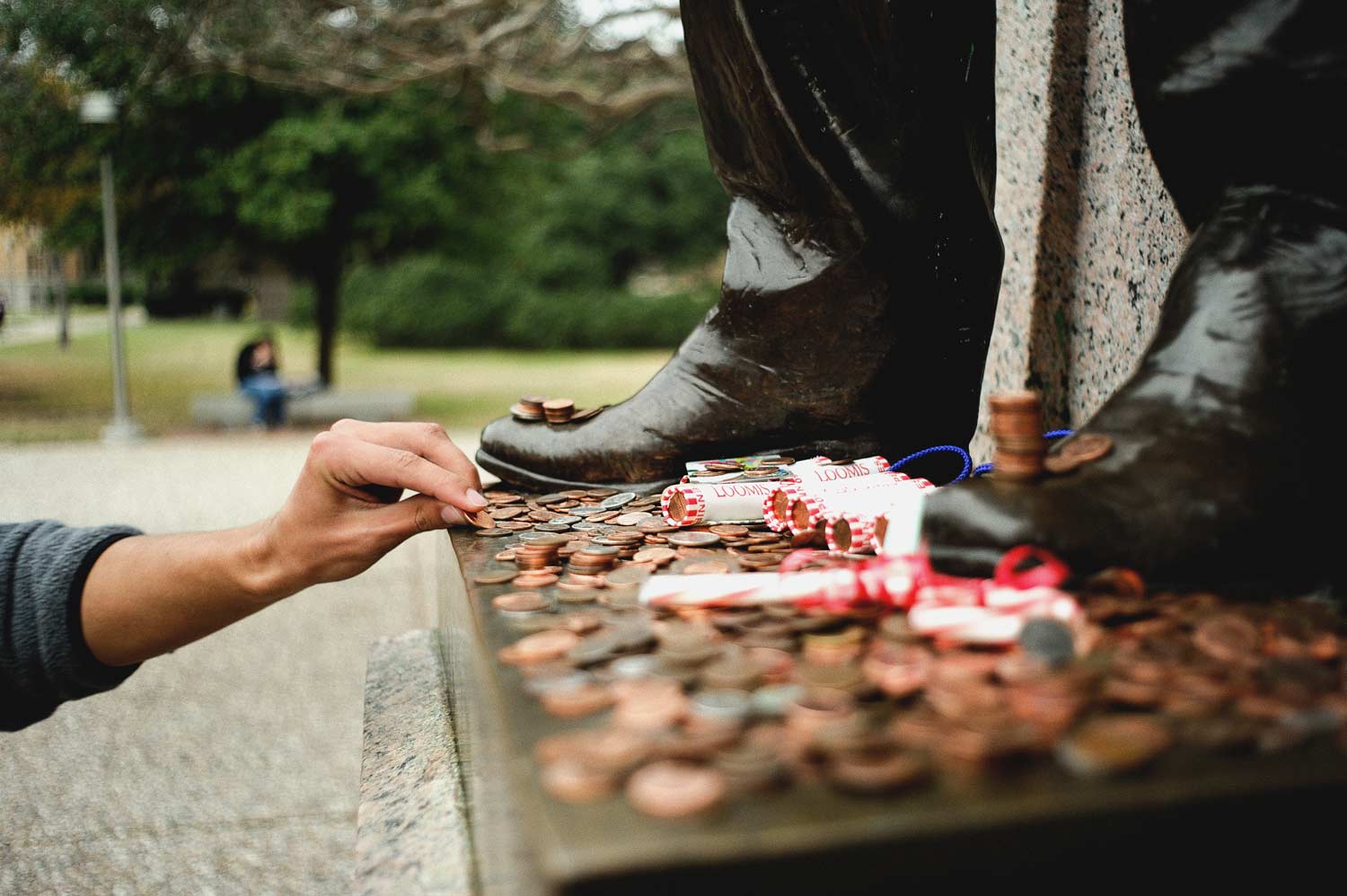 Student puts pennies on the base of the Sul Ross statue for good luck before a test