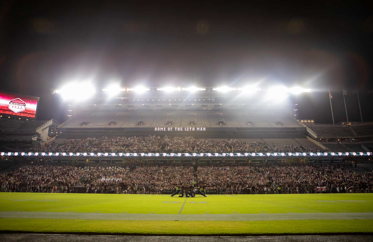 Yell leaders kneeling on Kyle Field in front of a crowded Kyle Field at Midnight Yell.
